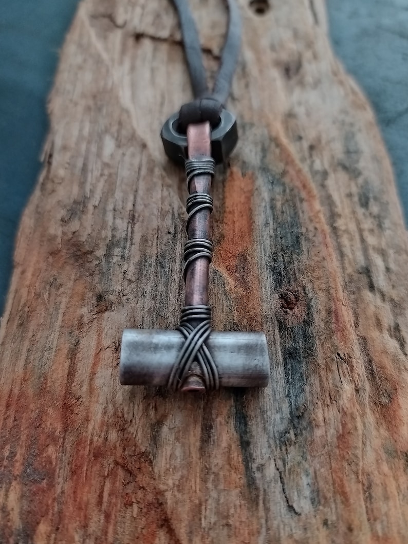 May include: A silver and copper hammer pendant necklace with a leather cord. The hammer is wrapped with copper wire.