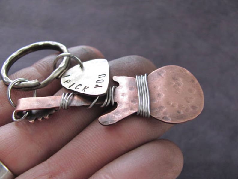 May include: A silver key chain with a copper guitar charm. The guitar charm has a hammered texture and the words "I pick you" are engraved on the pick.