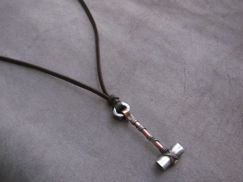 May include: A brown leather cord necklace with a silver and copper hammer pendant.