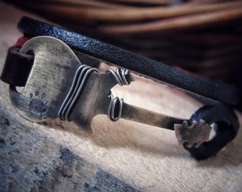 May include: A black leather bracelet with a silver and brass guitar charm. The charm has a paw print on it.