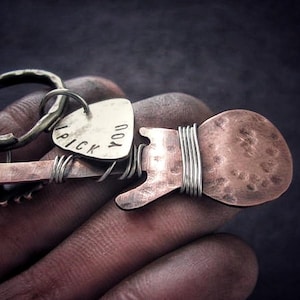 May include: A silver guitar pick keychain with the words "I pick you" engraved on it. The keychain is attached to a copper guitar-shaped charm with a hammered finish.
