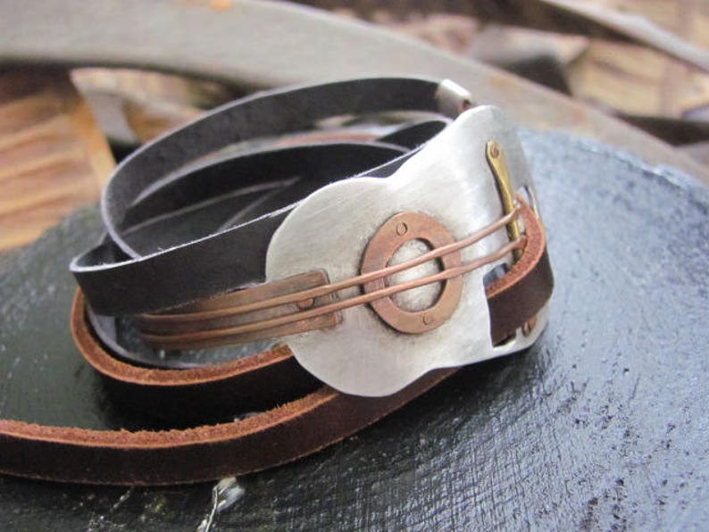 May include: A leather bracelet with a silver and copper guitar-shaped charm. The charm has a circular cutout with a smaller circle inside.