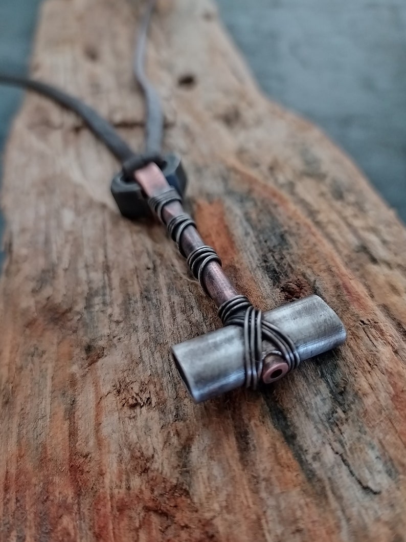 May include: A silver and copper wire wrapped pendant in the shape of a hammer, hanging from a black leather cord.