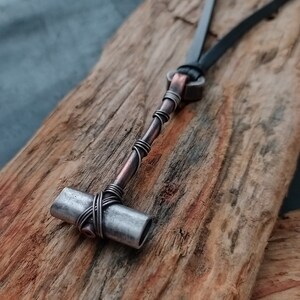 May include: A silver and copper wire wrapped pendant in the shape of a hammer, hanging from a black leather cord.