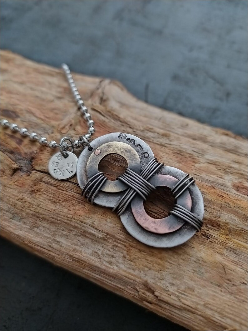 May include: A silver chain necklace with a pendant made of three metal rings. The rings are interlocked and have a copper and brass finish. The pendant is attached to a small silver charm with the word "Love" engraved on it.