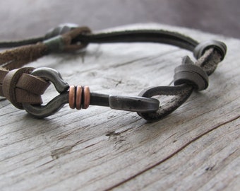 May include: A brown leather bracelet with a metal clasp and copper accents. The bracelet is tied with a knot.