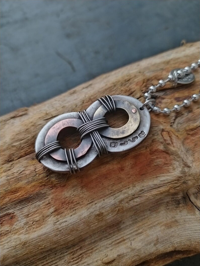 May include: A silver infinity symbol necklace with a copper and brass accent. The pendant is made of two intertwined circles with a wire wrapped around them. The necklace is on a silver chain.