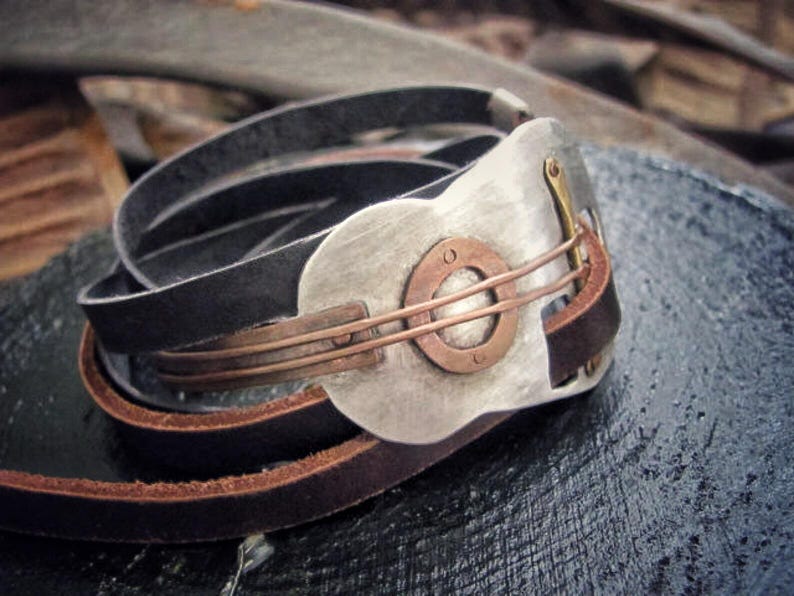 May include: A leather bracelet with a silver and copper guitar-shaped charm. The charm has a circular design with a copper center and a silver outer ring.