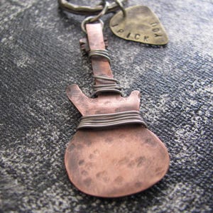 May include: A copper guitar-shaped keychain with silver wire wrapped around the body. The keychain has a small tag attached to it that says "Don't Pick".