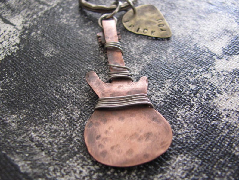May include: A copper guitar-shaped keychain with silver wire wrapped around the body. The keychain has a small tag attached to it that says "Don't Pick".