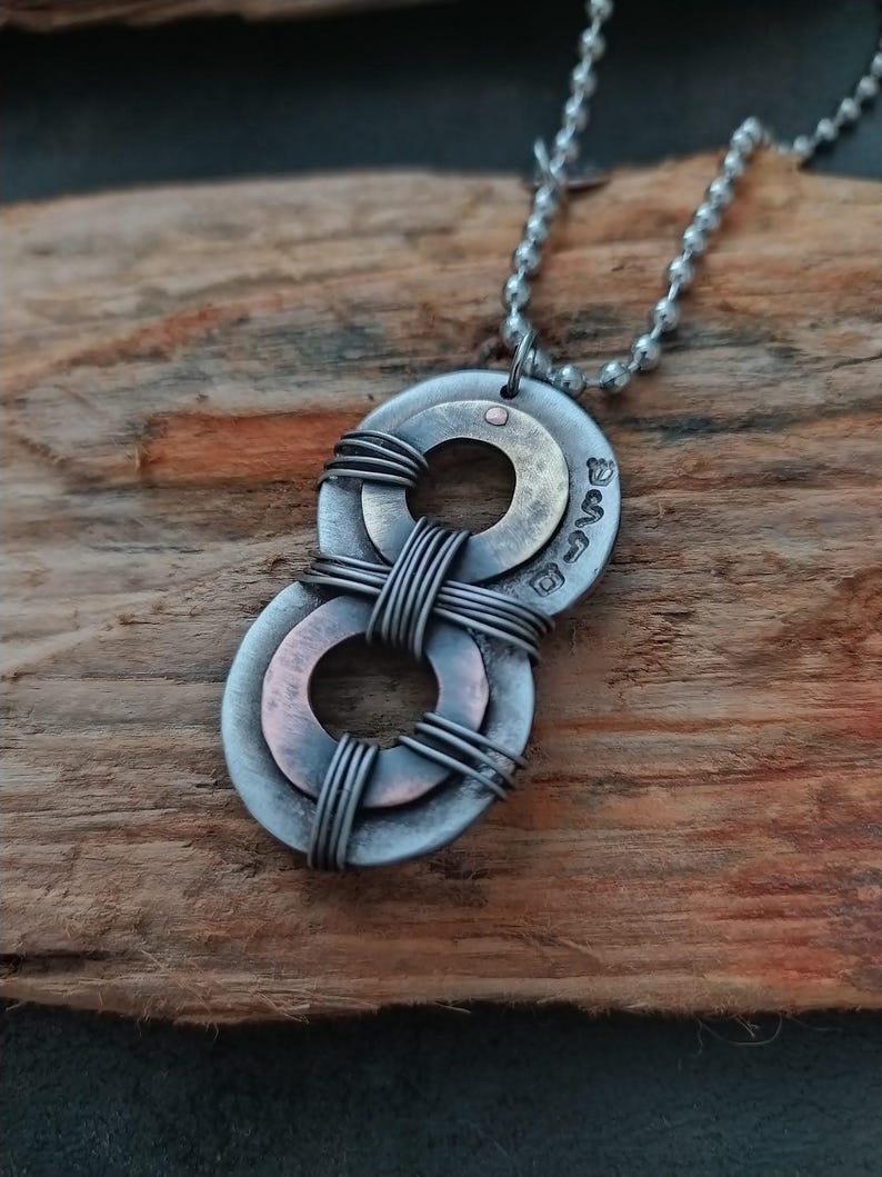 May include: A silver necklace with a pendant made of two stacked metal washers. The washers are connected by wire and have a copper finish. The pendant is inscribed with the word "Love".