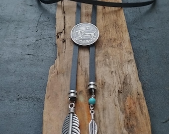 Puede incluir: Un corbatín bolo de cuero negro con un colgante de moneda de plata que presenta un león y texto en hebreo. La corbata también tiene dos dijes de plumas plateadas y una cuenta turquesa.
