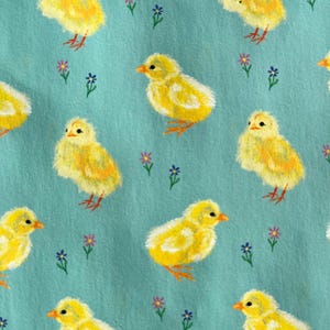 Peut inclure: Motif r&eacute;p&eacute;t&eacute; de poussins jaunes avec des becs et des pattes orange sur fond bleu clair. De petites fleurs violettes et bleues sont dispers&eacute;es dans le motif. Les poussins sont peints avec un effet de coups de pinceau textur&eacute;s.