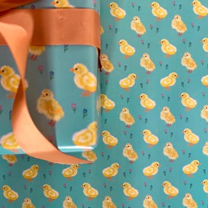 Peut inclure: Papier cadeau avec un motif r&eacute;p&eacute;t&eacute; de poussins jaunes sur fond turquoise et de petites fleurs violettes. Un ruban p&ecirc;che est nou&eacute; autour du cadeau emball&eacute;, pour une touche d&eacute;corative.