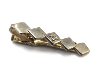 May include: A gold tie clip with a row of five diamond-shaped pieces. The center piece has a small clear rhinestone.