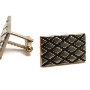 May include: A pair of gold-toned cufflinks with a geometric diamond pattern. The rectangular cufflinks have a textured surface and a classic post closure. The design features a series of intersecting lines creating a diamond grid.
