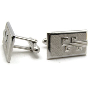 May include: A pair of silver cufflinks with a geometric design. The cufflinks are rectangular in shape and have a brushed finish.