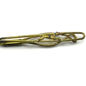 May include: A gold-toned tie clip with a stylized running dog design. The dog is outlined in black and has blue accents.