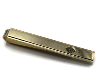 May include: A gold tie clip with a black diamond-shaped design.