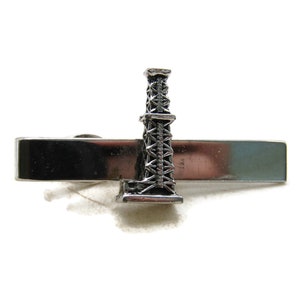 May include: A silver-toned tie bar featuring a detailed miniature oil derrick. The derrick is intricately designed, standing upright on a rectangular bar. The tie bar is a classic accessory for formal wear.