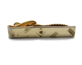 May include: A gold tie clip with a diamond-shaped design and a single clear rhinestone in the center. The clip has a textured, striped pattern.