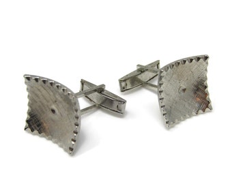 May include: A pair of silver cufflinks with a textured, geometric design. The cufflinks have a square shape with rounded corners and a raised center.