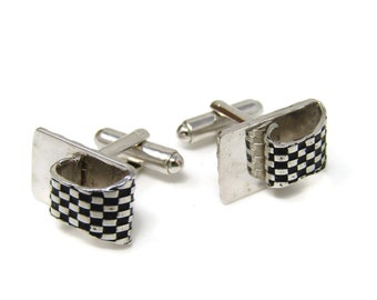 May include: A pair of silver-toned cufflinks with a rectangular base and a curved, flag-like design. The flag features a black and white checkered pattern, adding a classic touch to the accessory.