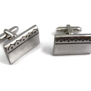 May include: A pair of silver cufflinks with a decorative border design.
