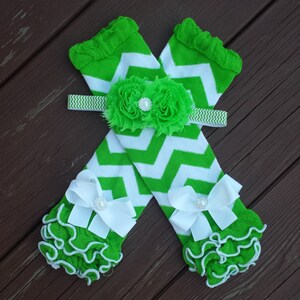 Può includere: Scaldamuscoli a chevron verde e bianco con volant bianchi e fiocchi bianchi con centri di perle. È incluso un cerchietto a chevron verde e bianco con un fiore verde con un centro di perla.
