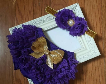 May include: Purple lace baby bloomers with a gold glitter bow and a matching purple flower headband with a gold glitter band and a pearl accent.