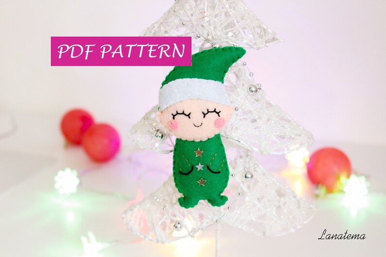 May include: PDF pattern for a felt Christmas elf ornament. The elf is wearing a green hat and a green and white outfit with gold stars. The elf has a smiling face with closed eyes.
