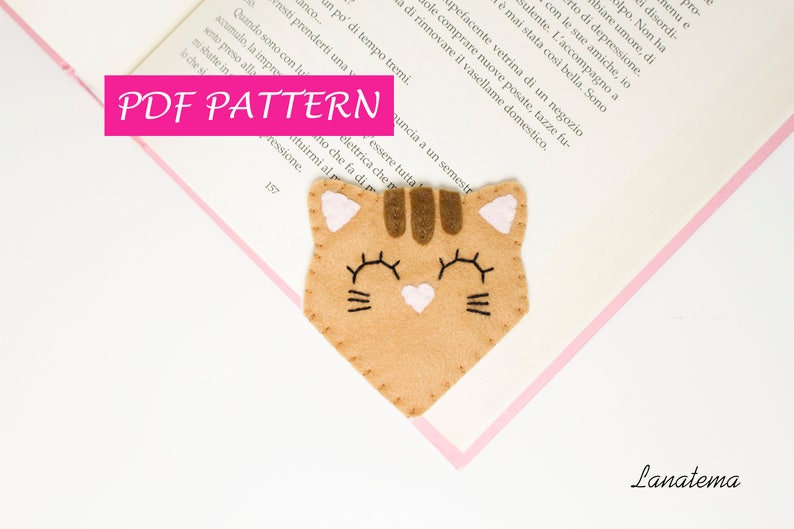 May include: A PDF pattern for a felt cat bookmark. The cat is brown with pink ears and a pink heart on its chest. The pattern includes instructions for sewing the bookmark.