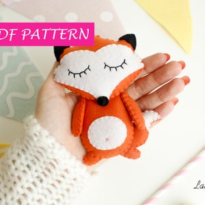 May include: A PDF pattern for sewing a small orange felt fox with white felt accents. The fox has closed eyes and a white felt belly. The pattern is available for download.