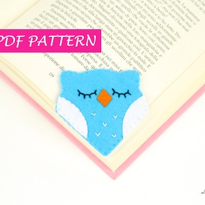 May include: A PDF pattern for a blue felt owl bookmark with white wings and orange beak. The pattern is on a book with the text "PDF PATTERN" in pink.
