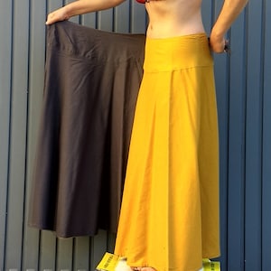 Op de afbeelding: Twee lange rokken, een donkergrijs en een felgeel, worden door een persoon omhoog gehouden. De rokken zijn gemaakt van een zachte, vloeiende stof.