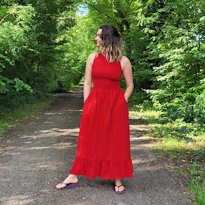 Può includere: Una donna che indossa un abito maxi rosso con un orlo a balze, in piedi su un sentiero in un bosco.