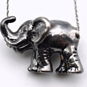 May include: A silver-toned elephant pendant necklace. The elephant is detailed with textured skin and a raised trunk. The pendant hangs from a delicate silver chain. The elephant is approximately 1.5 inches long.