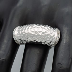 May include: A silver ring with a hammered texture and a row of small clear stones around the band.