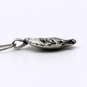 May include: Silver-toned pendant necklace with a detailed, ornate design. The pendant is a small, shallow dish shape with intricate patterns. The necklace chain is a thin, silver snake chain. The pendant is approximately 1 inch in length.