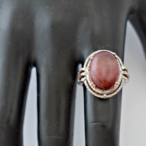 May include: A silver ring with a large oval-shaped red gemstone set in a silver and rose gold bezel. The ring has a decorative design around the gemstone.