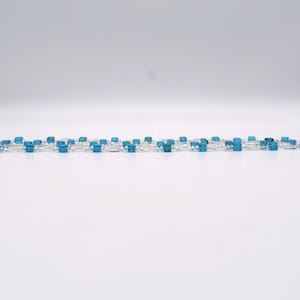 Op de afbeelding: Een zilveren ketting met afwisselend heldere en blauwe vierkante kralen.