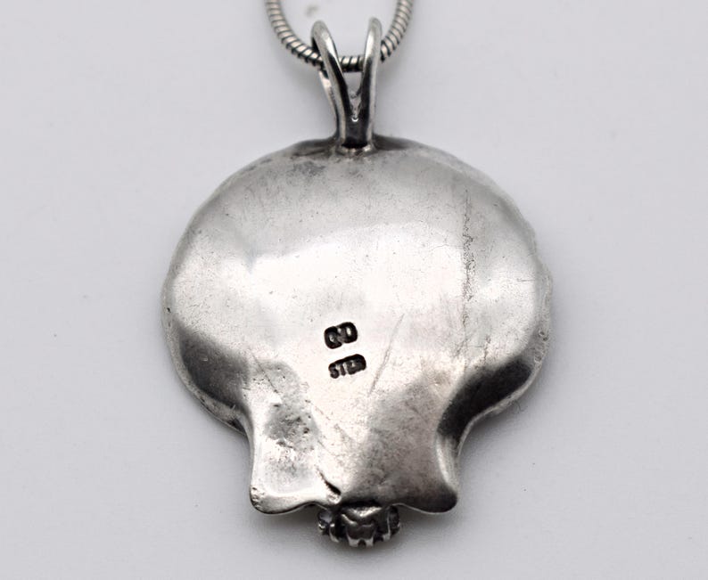 May include: A silver pendant with a pomegranate design, attached to a silver chain. The pendant has a textured surface and a small, detailed base. The back of the pendant has the markings "GD" and "STER".