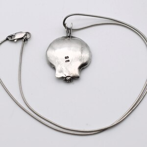 May include: A silver pendant necklace featuring a pomegranate-shaped pendant. The pendant is detailed with a textured surface and a small gemstone at the base. The necklace has a delicate, snake chain and a secure clasp.