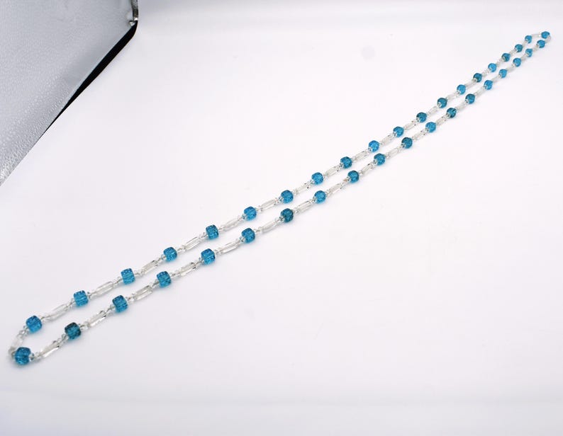 Op de afbeelding: Een zilveren ketting met blauwe edelsteen kralen. De kralen zijn vierkant en hebben een gefacetteerd oppervlak.
