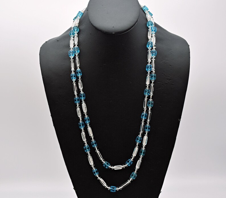 Op de afbeelding: Een dubbele ketting met heldere en blauwe glazen kralen. De kralen zijn ovaalvormig en hebben een facetgeslepen ontwerp.