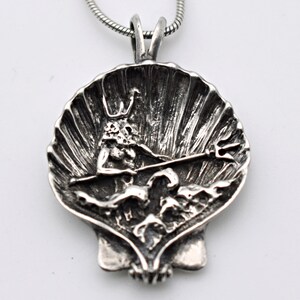 May include: A silver pendant necklace featuring a detailed seashell design. Inside the shell is a sculpted figure holding a trident. The pendant is attached to a silver chain, creating a nautical-themed accessory.