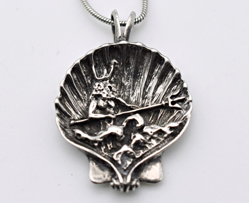 May include: A silver pendant necklace featuring a detailed seashell design. Inside the shell is a sculpted figure holding a trident. The pendant is attached to a silver chain, creating a nautical-themed accessory.
