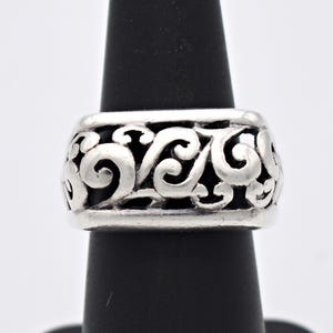 May include: A silver ring with an openwork design featuring swirling, scroll-like patterns. The ring is wide and has a band of approximately 2.5 cm. The ring is displayed on a black ring holder against a white background.