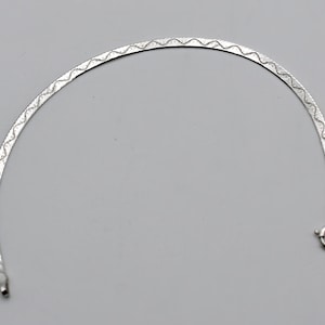 May include: A silver-toned herringbone chain bracelet featuring a delicate, repeating wavy line pattern etched along the center of the flat, flexible links. The bracelet is finished with a small, circular spring ring clasp at one end.