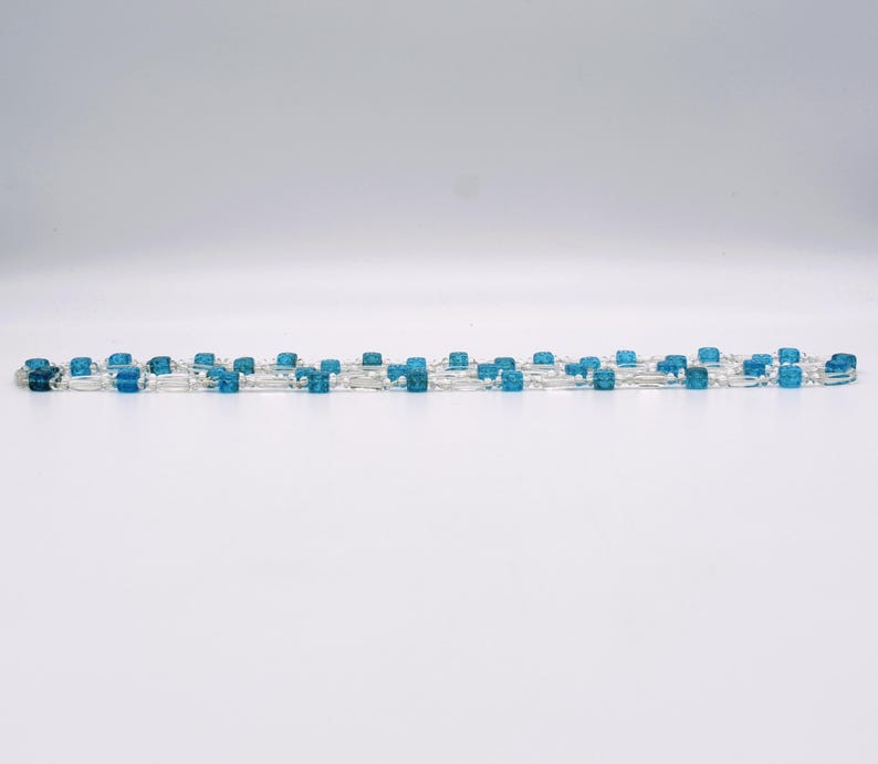 Op de afbeelding: Een lange streng blauwe en heldere glazen kralen. De kralen zijn vierkant en hebben een matte afwerking.
